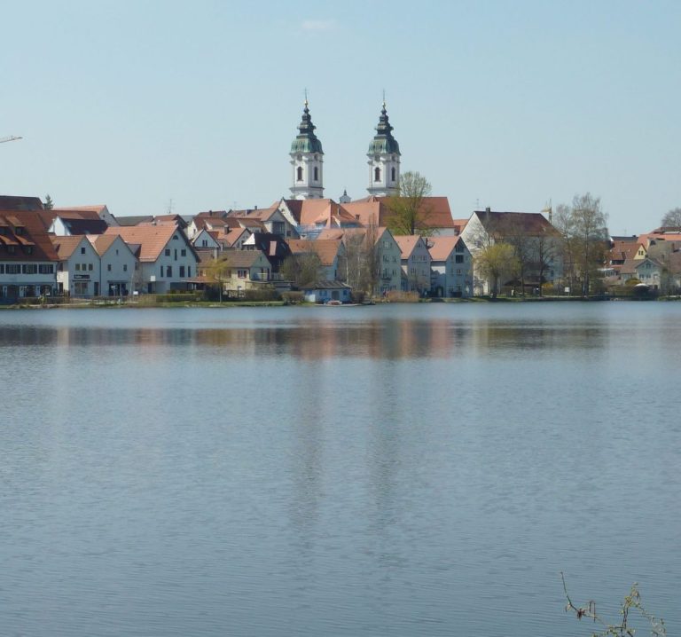 Blick über den Stadtsee in Bad Waldsee Stadtansicht mit Wasserreflexionen und zwei markanten Kirchtürmen.